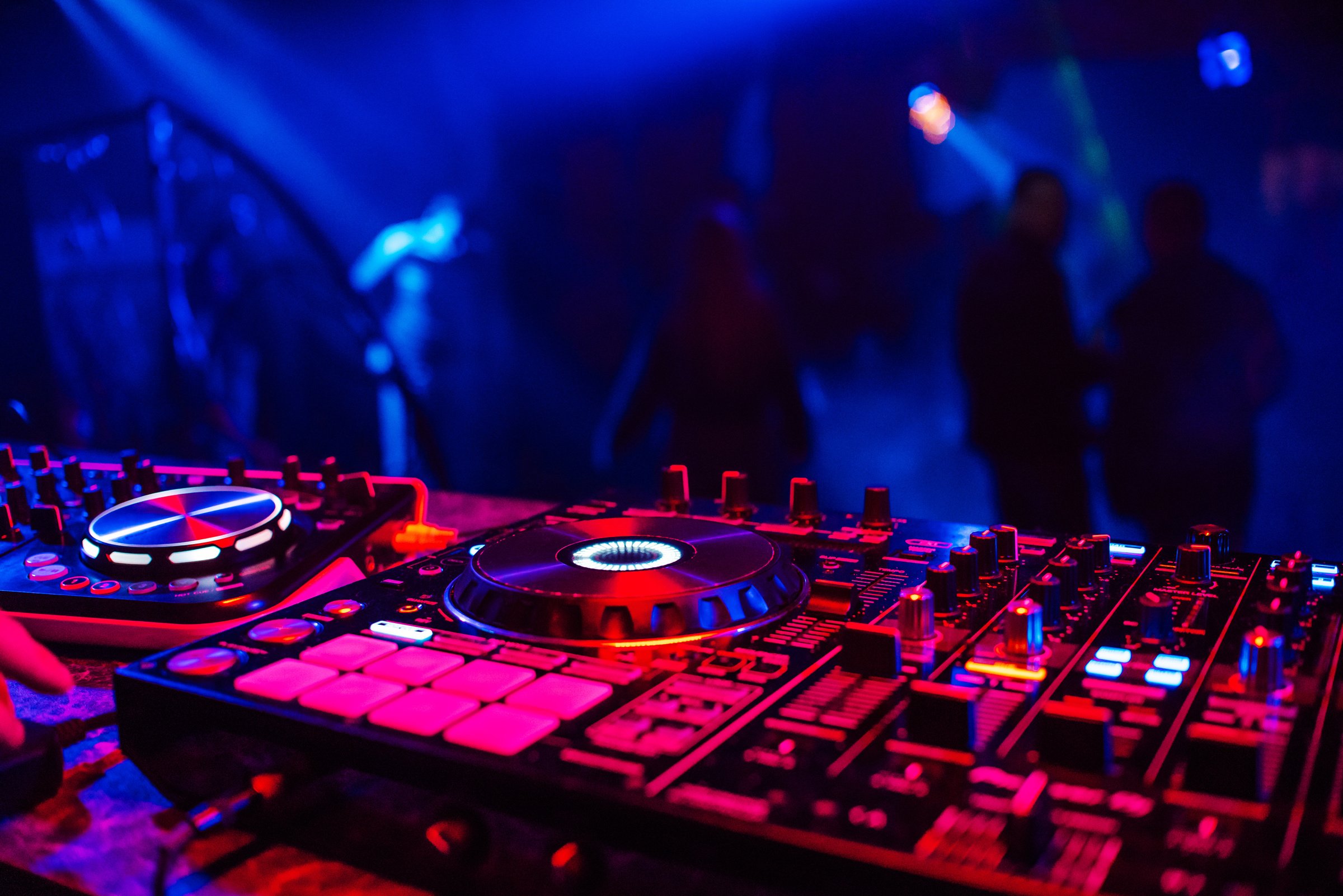 DJ Console for Mixing Music with Blurry People Dancing at a Nightclub Party